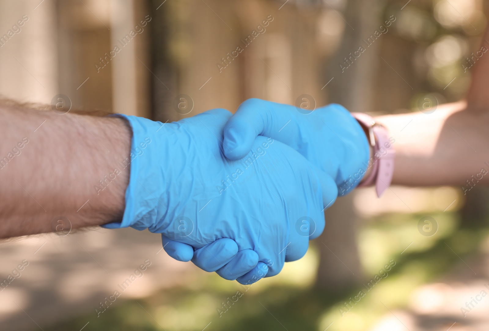 Photo of Man and woman in protective gloves shaking hands to say hello outdoors, closeup
