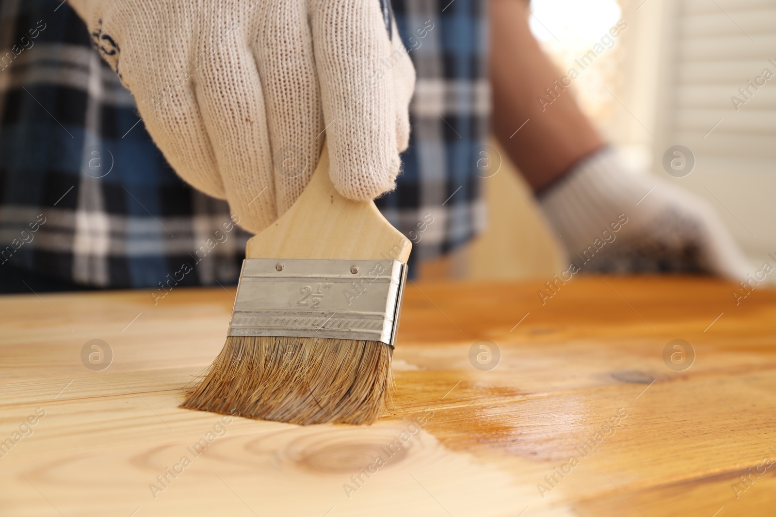 Photo of Man with brush applying wood stain onto wooden surface indoors, closeup