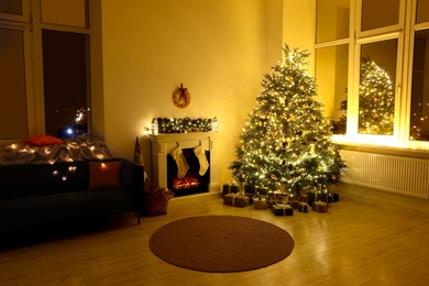 Stylish fireplace near Christmas tree, sofa and accessories in cosy room