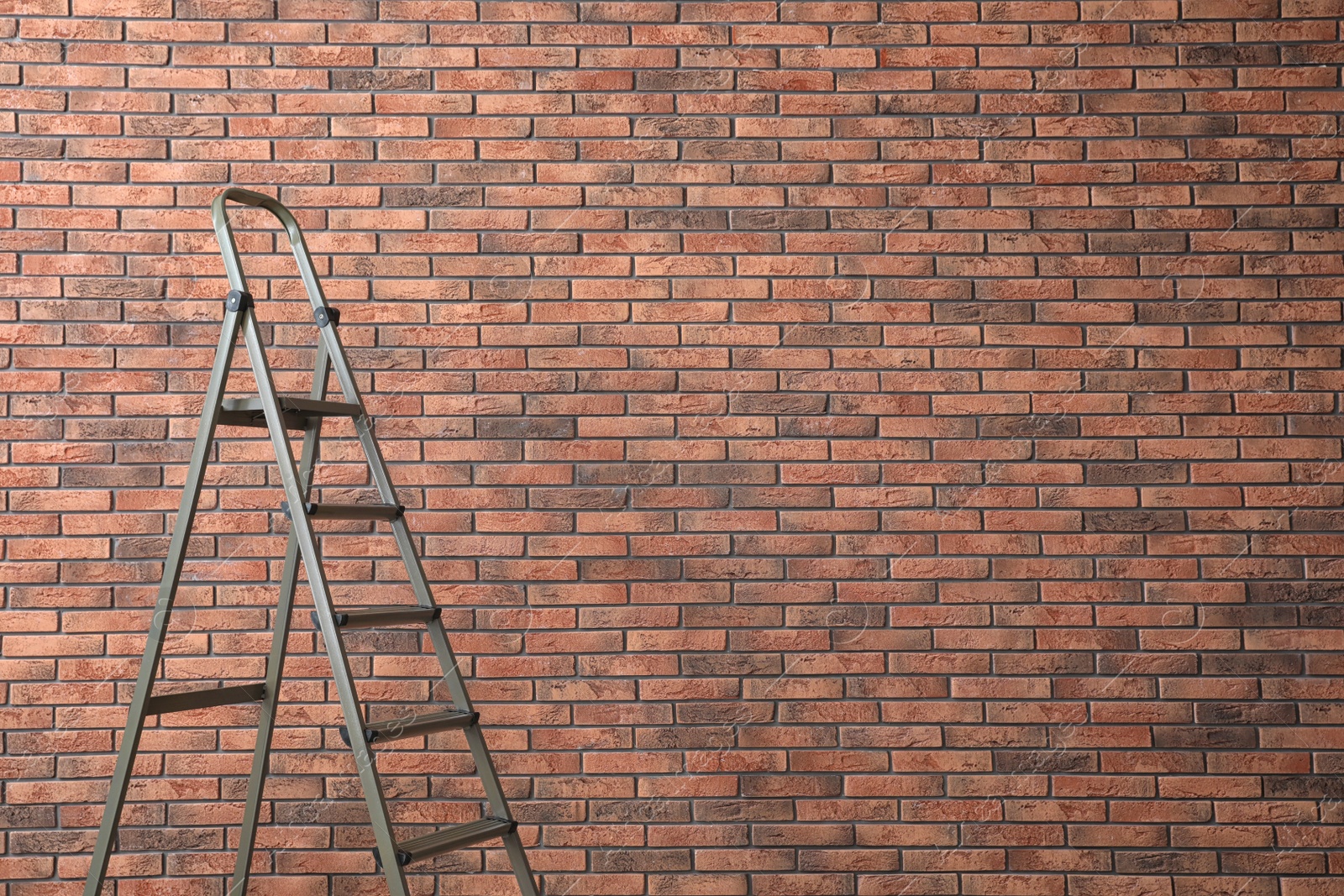 Photo of Metal stepladder near brick wall. Space for text