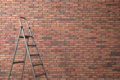 Metal stepladder near brick wall. Space for text