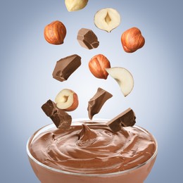 Image of Making yummy chocolate paste. Hazelnuts and pieces of chocolate falling into bowl on light blue background