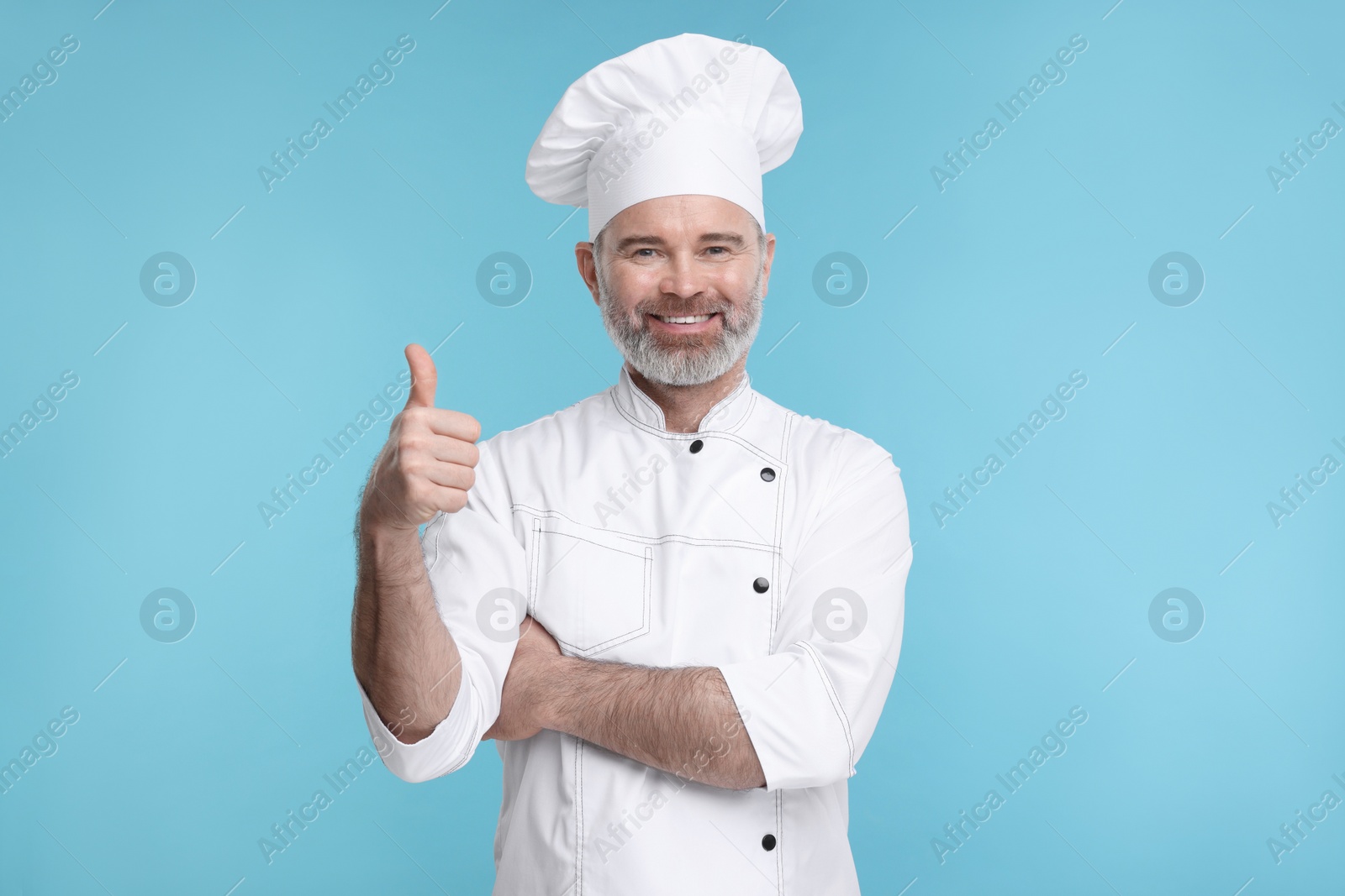 Photo of Happy chef in uniform showing thumbs up on light blue background