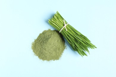 Photo of Pile of wheat grass powder and fresh sprouts on light blue table, flat lay