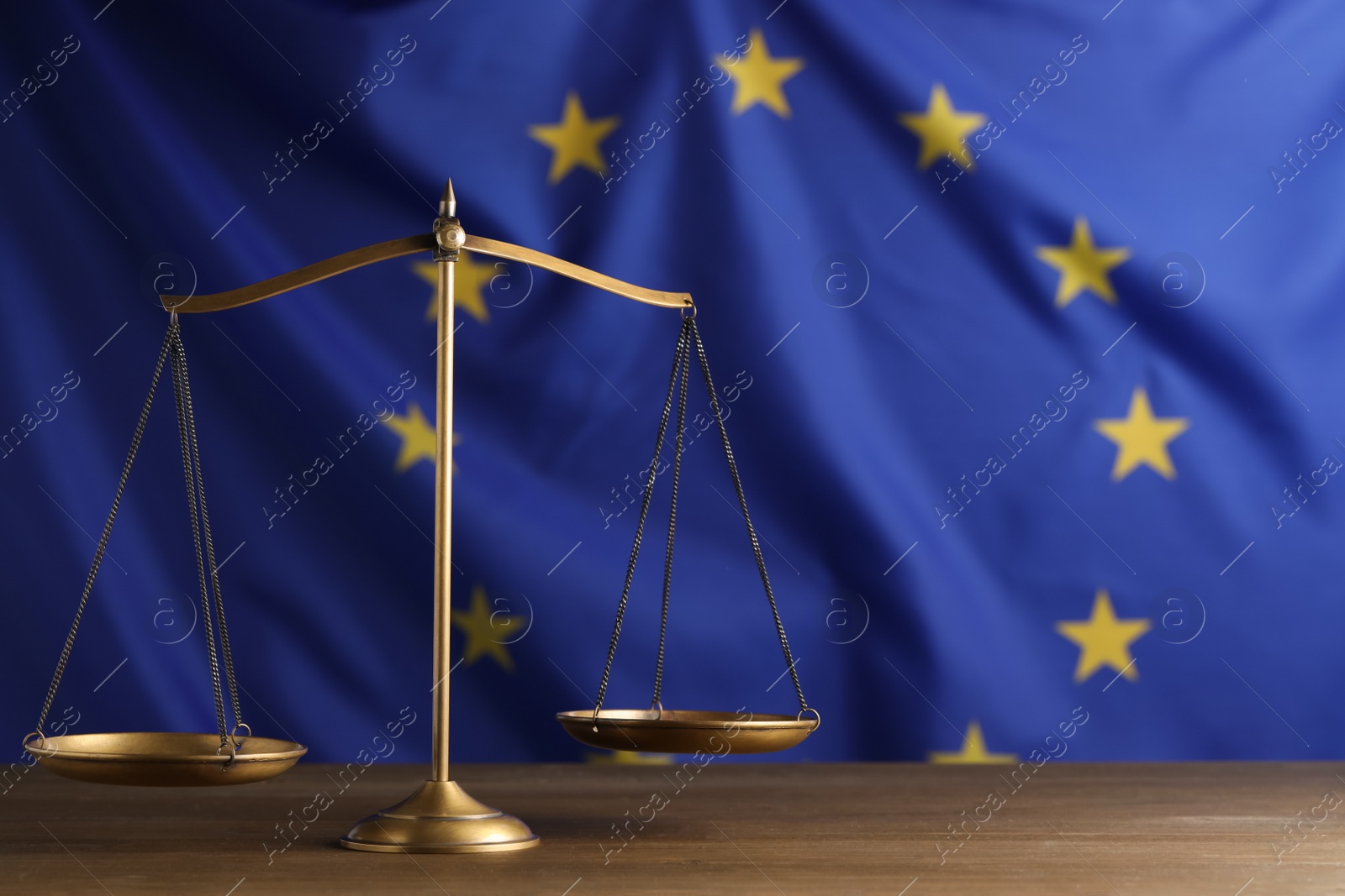 Photo of Scales of justice on wooden table against European Union flag. Space for text