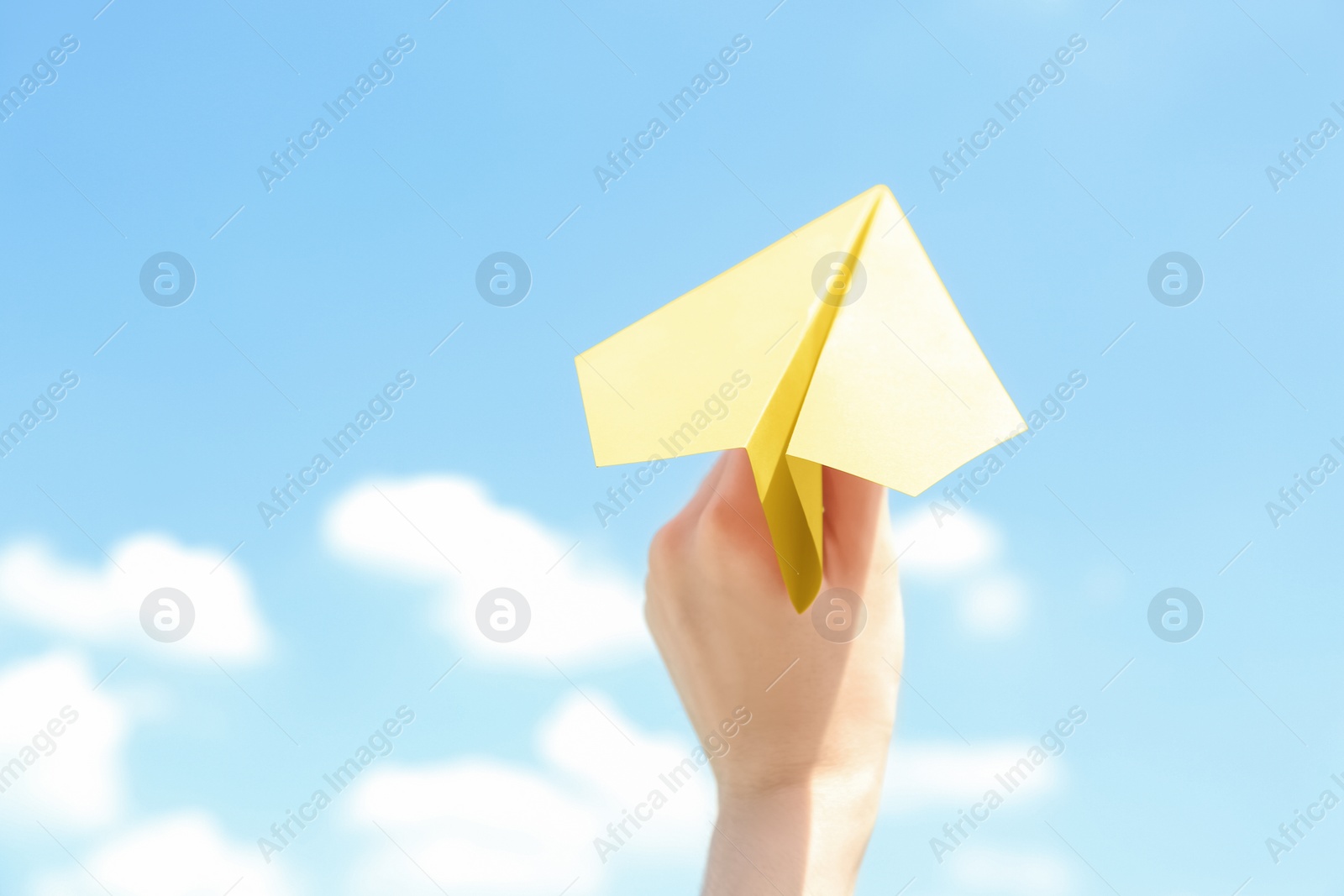 Photo of Woman holding paper plane against blue sky, closeup. Space for text