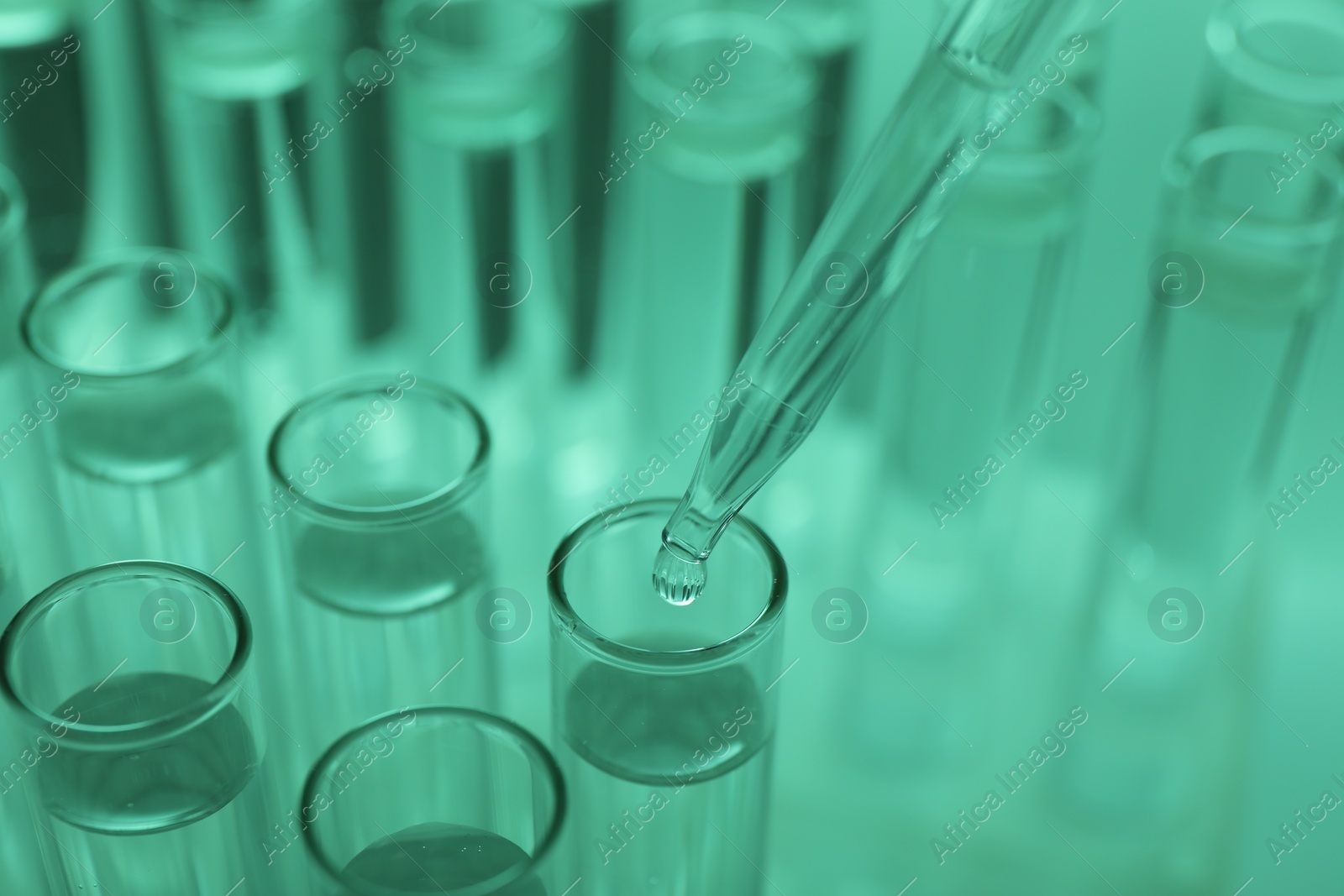 Photo of Dripping liquid from pipette into test tube on green background, closeup