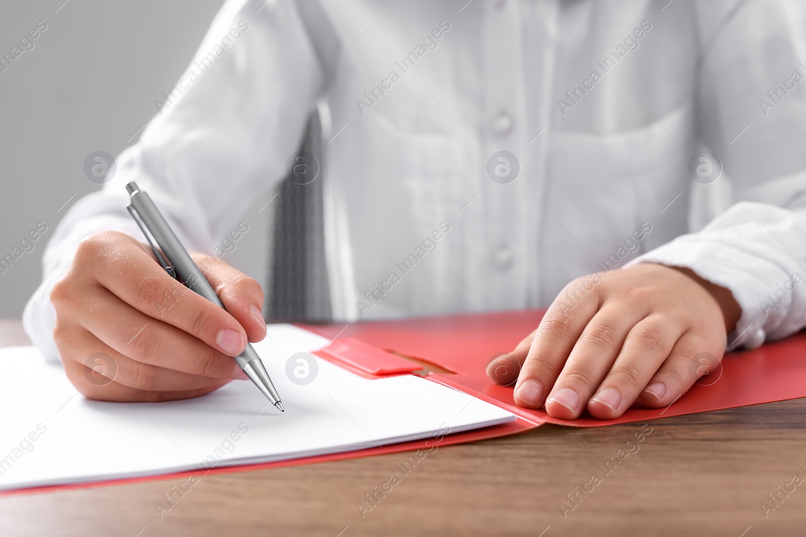 Photo of Woman writing on sheet of paper in red folder at wooden table in office, closeup