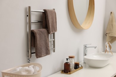 Photo of Heated towel rail with brown towels in bathroom