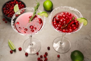 Photo of Tasty cranberry cocktail with rosemary and lime in glasses on grey table, closeup