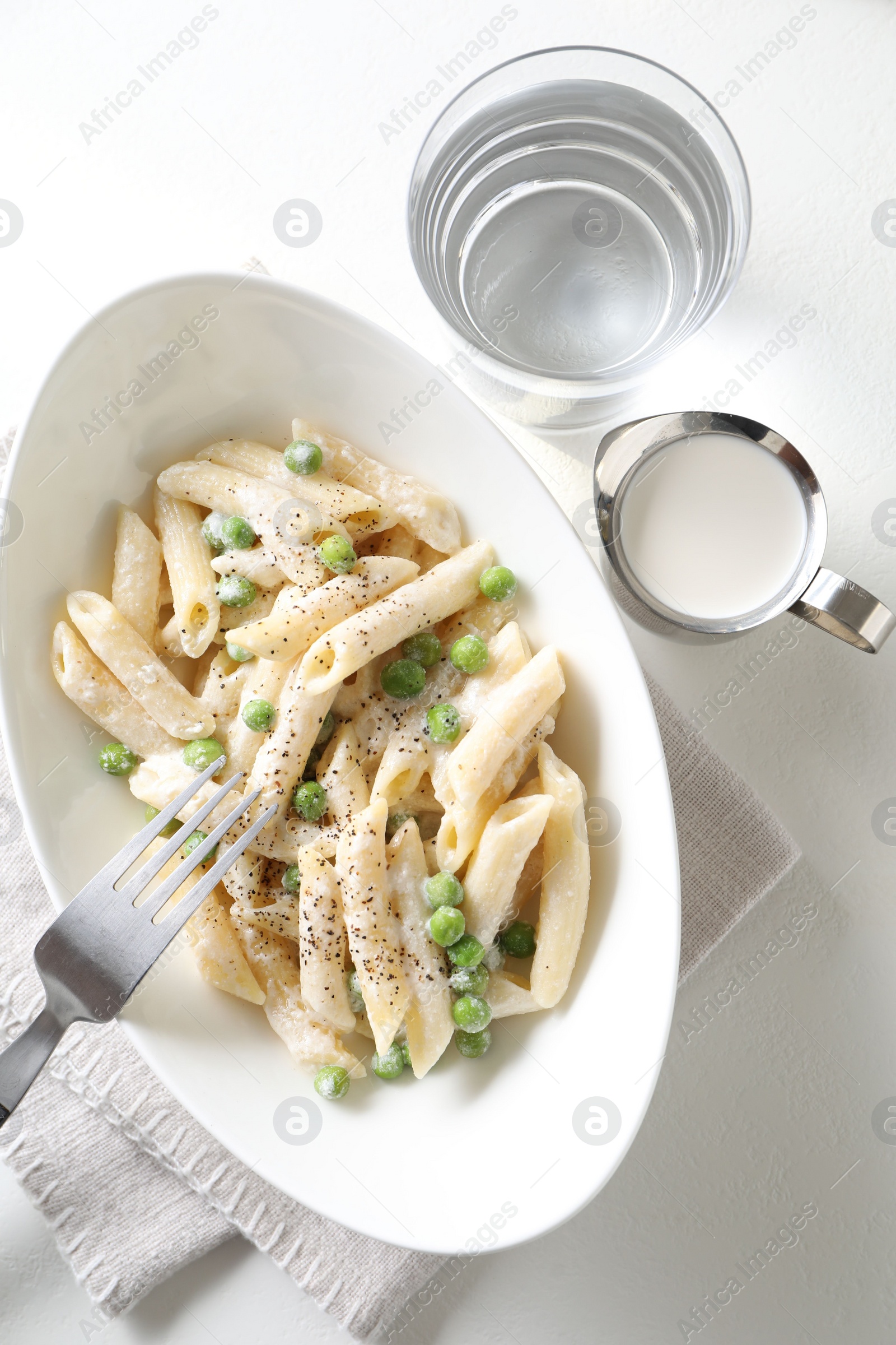 Photo of Delicious pasta with green peas, creamy sauce, water and fork on white table, top view