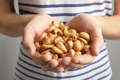 Photo of Woman holding cashew nuts on light background, closeup