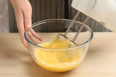 Photo of Woman beating eggs with mixer at wooden table, closeup