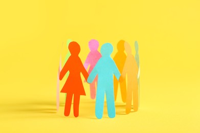 Photo of Many different paper human figures standing in circle on yellow background. Diversity and inclusion concept