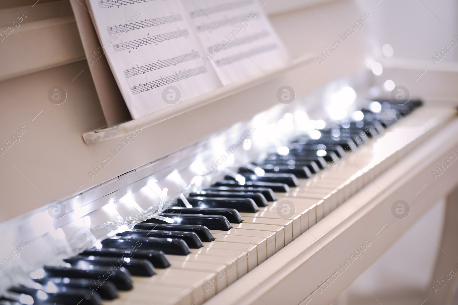 Photo of Glowing fairy lights on piano keys, closeup. Christmas music