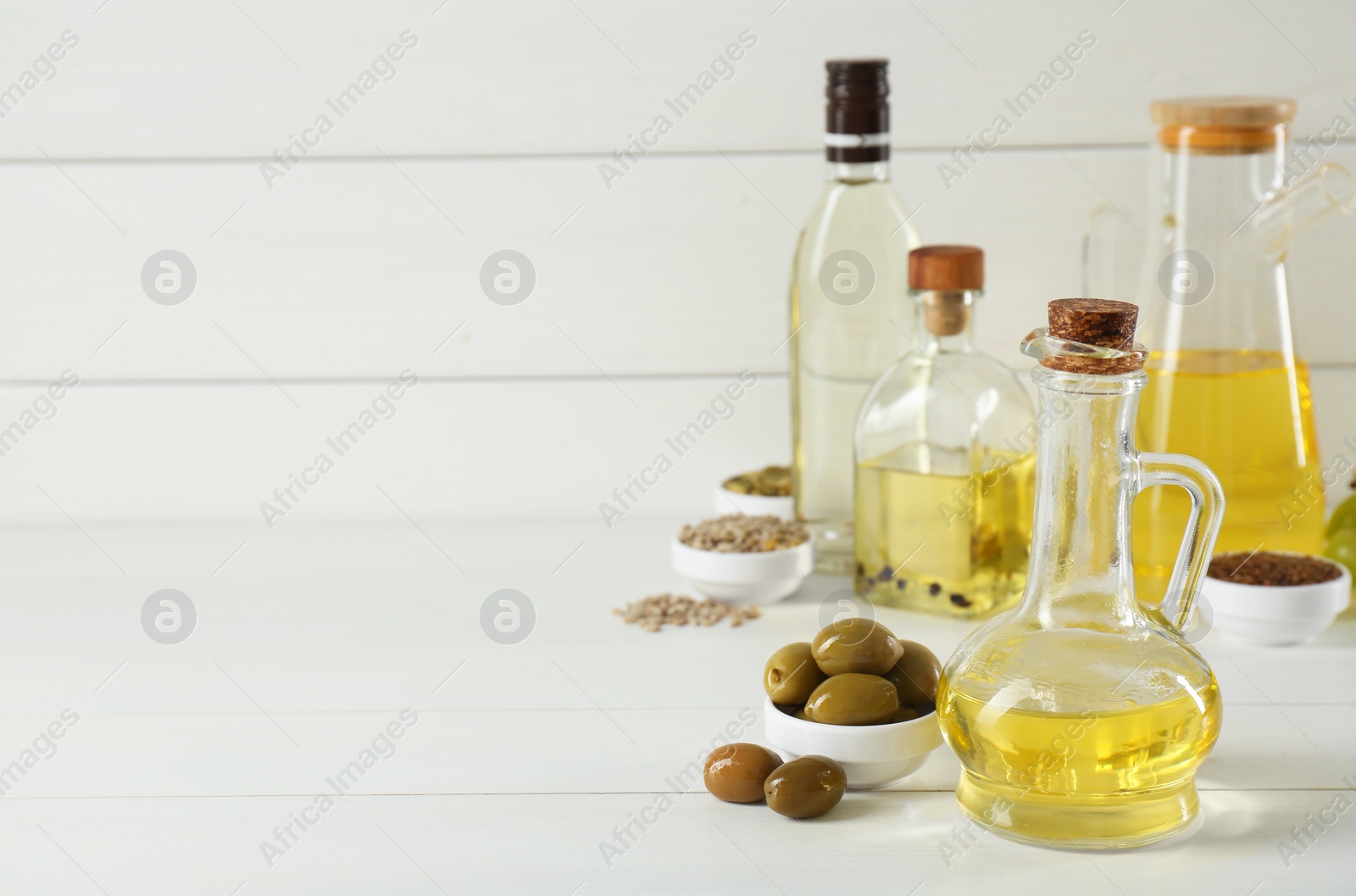 Photo of Vegetable fats. Different cooking oils in bottles and ingredients on white wooden table, space for text