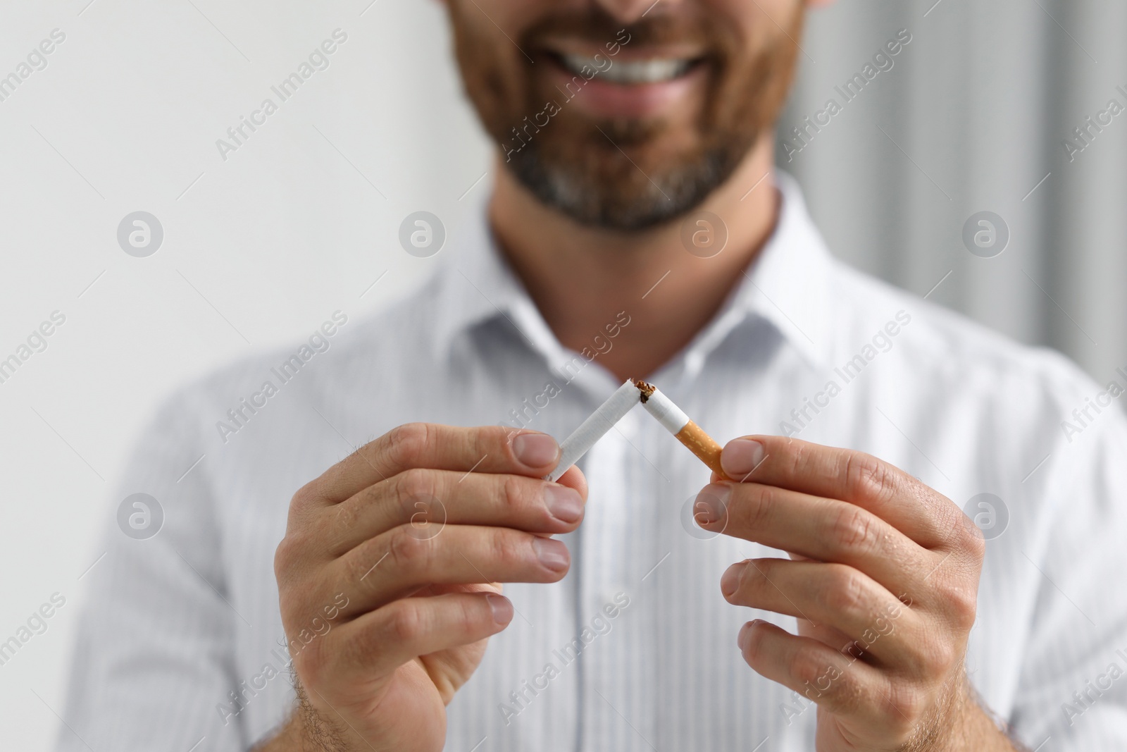 Photo of Stop smoking concept. Man breaking cigarette on light background, closeup