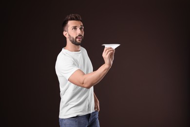 Handsome man playing with paper plane on brown background