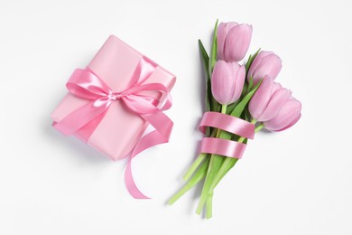 Beautiful gift box with pink bow and tulips on white background, flat lay