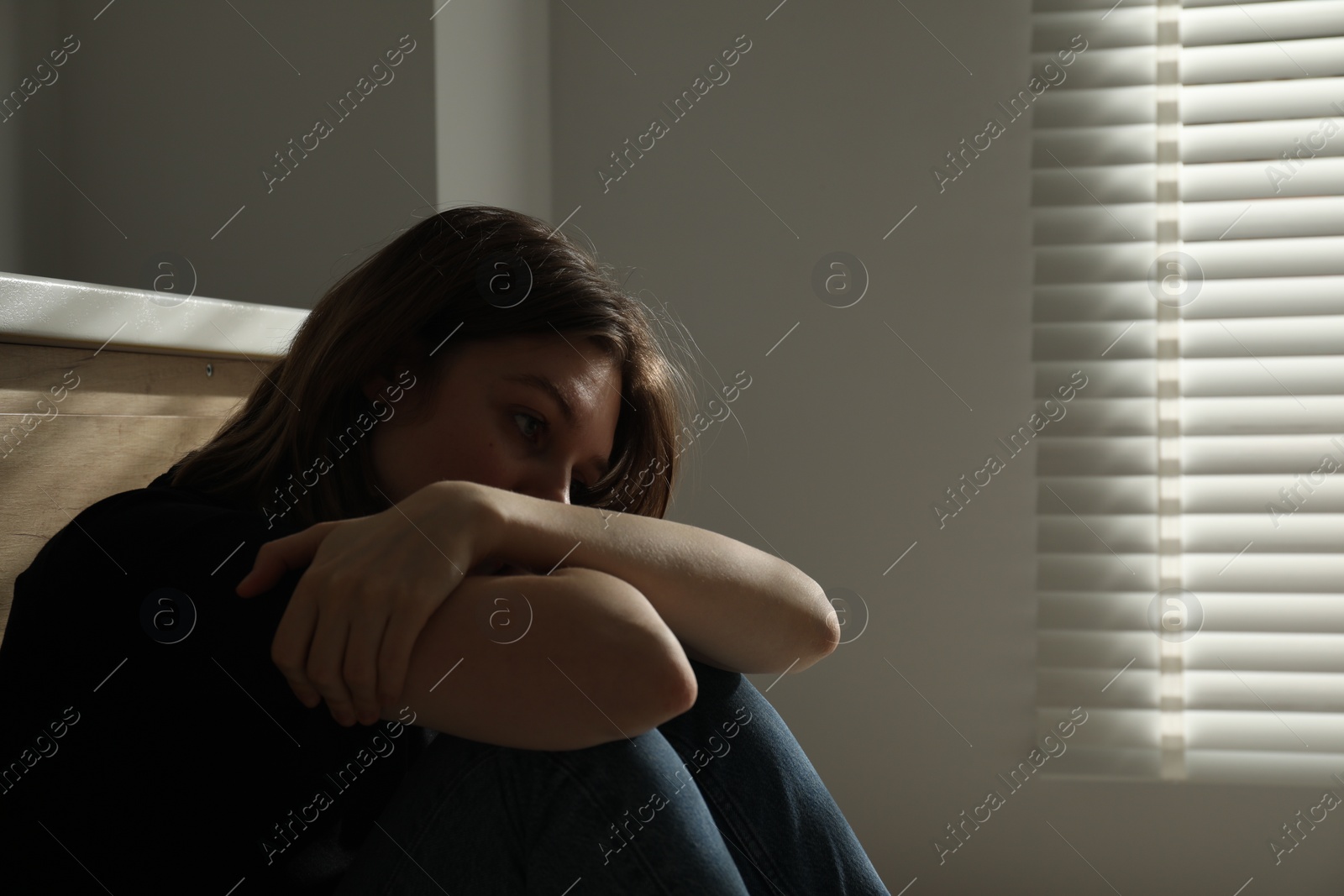 Photo of Sad young woman sitting indoors, space for text