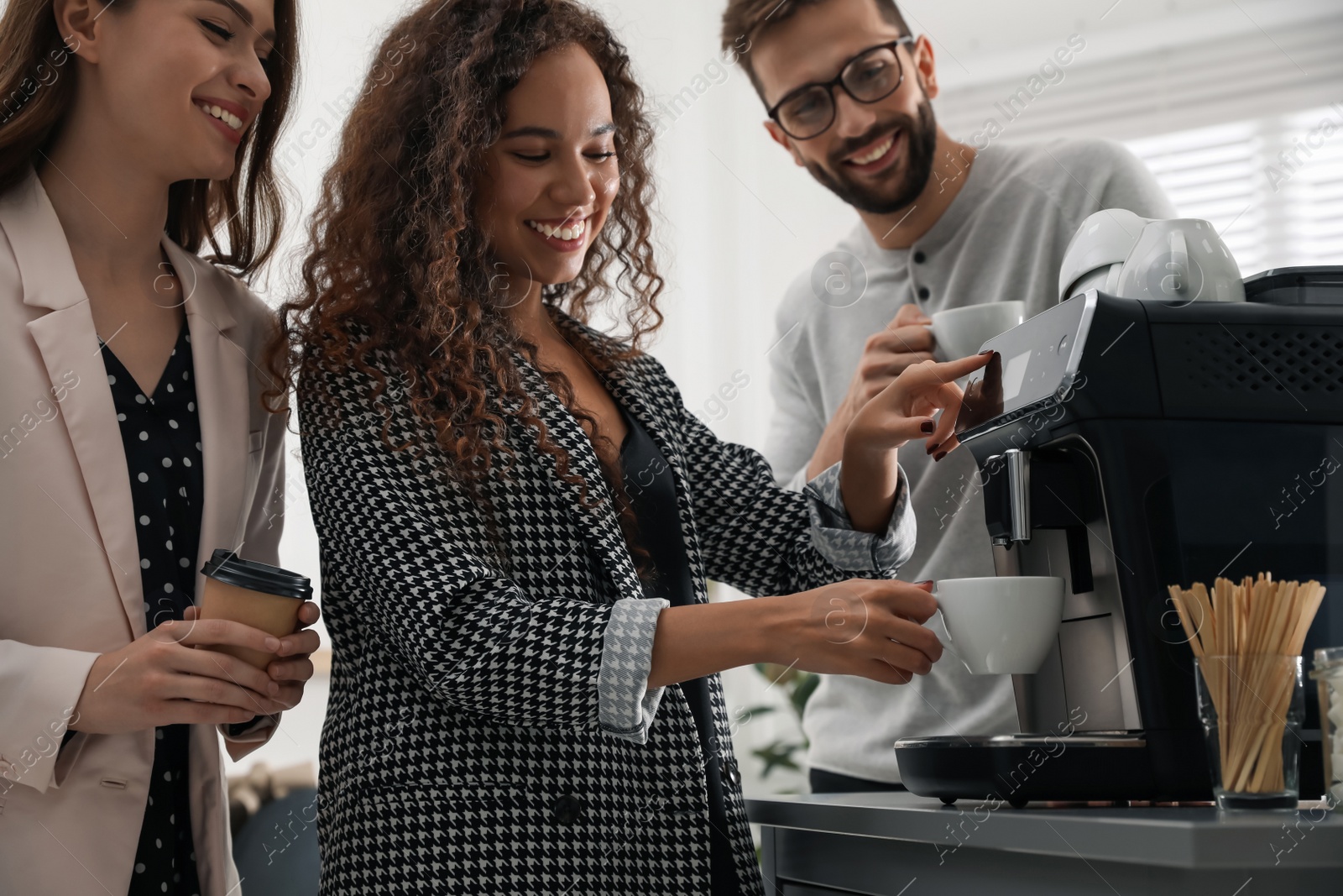 Photo of African American woman talking with colleagues while using modern coffee machine in office