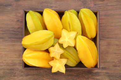 Photo of Cut and whole delicious ripe carambolas in box on wooden table, top view