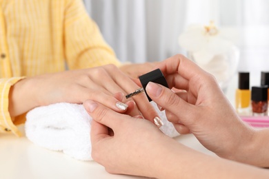 Photo of Manicurist painting client's nails with polish in salon, closeup