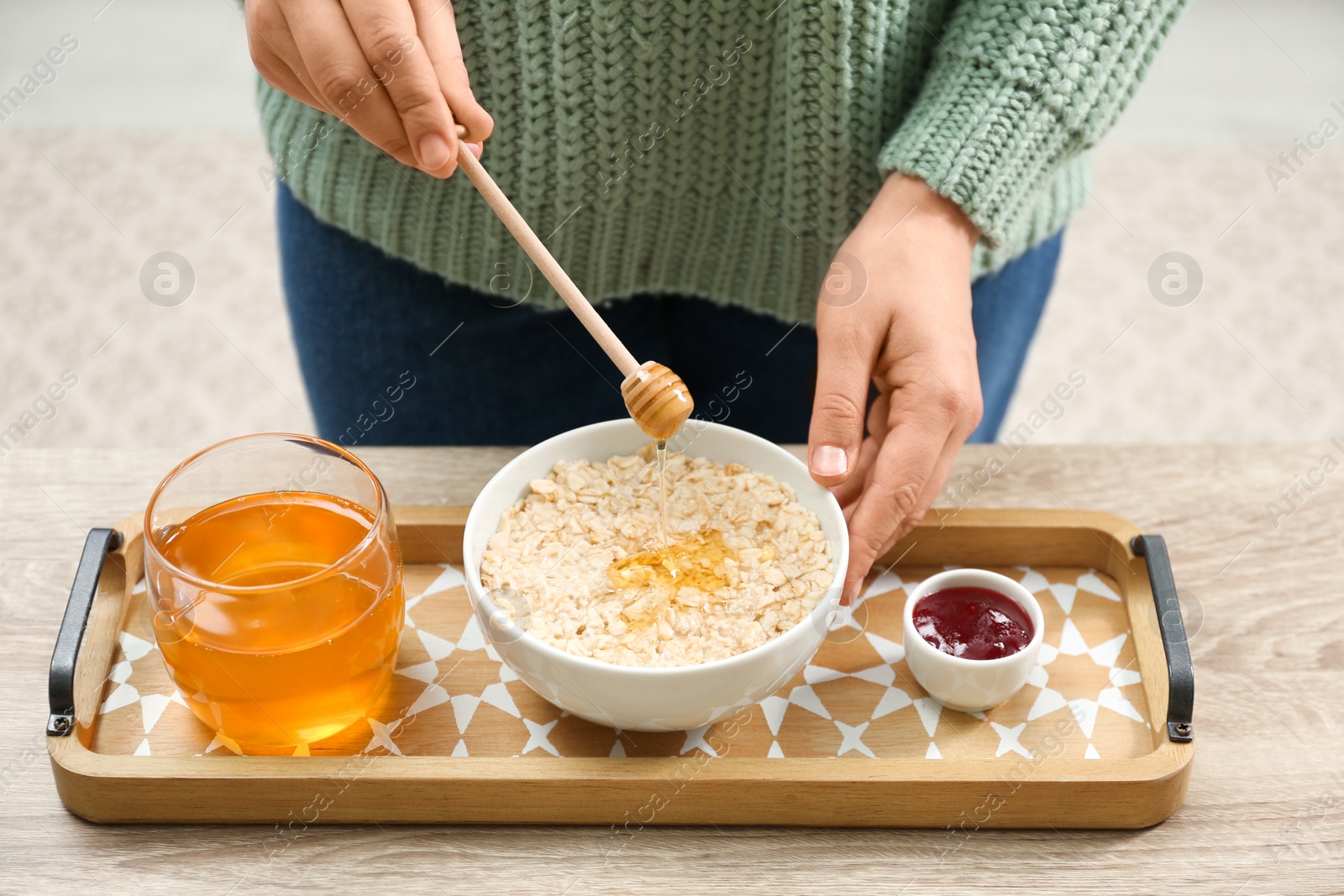 Photo of Woman adding honey to oatmeal at wooden table, closeup