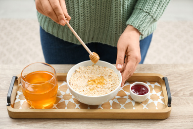 Photo of Woman adding honey to oatmeal at wooden table, closeup