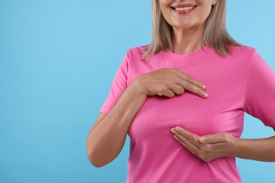 Woman doing breast self-examination on light blue background, closeup. Space for text