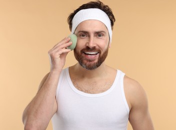 Man with headband washing his face using sponge on beige background