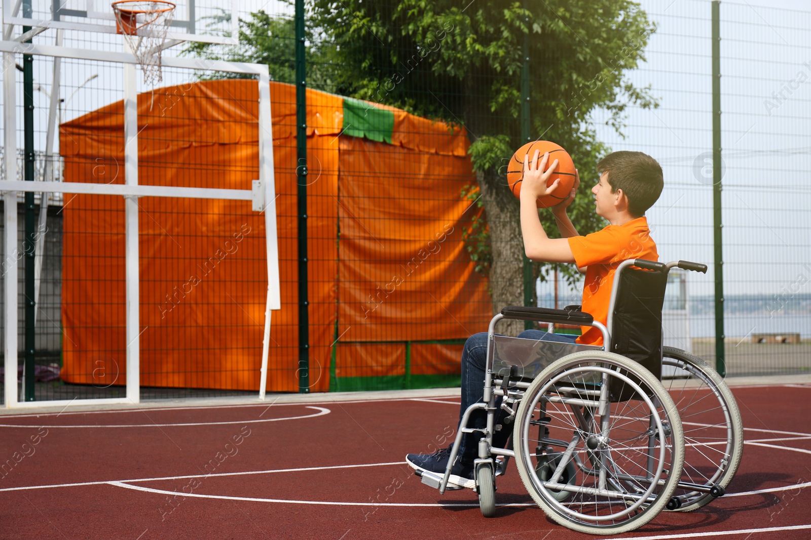 Photo of Disabled teenage boy in wheelchair playing basketball  on outdoor court