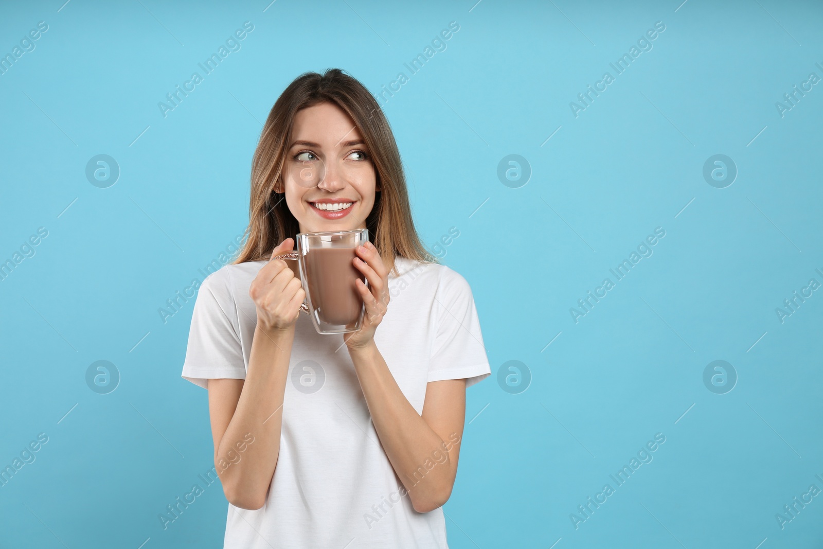 Photo of Young woman drinking chocolate milk on light blue background. Space for text