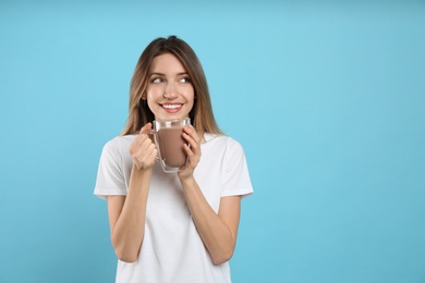 Photo of Young woman drinking chocolate milk on light blue background. Space for text