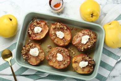 Photo of Tasty baked quinces with nuts, cream cheese and honey in dish on white marble table, flat lay