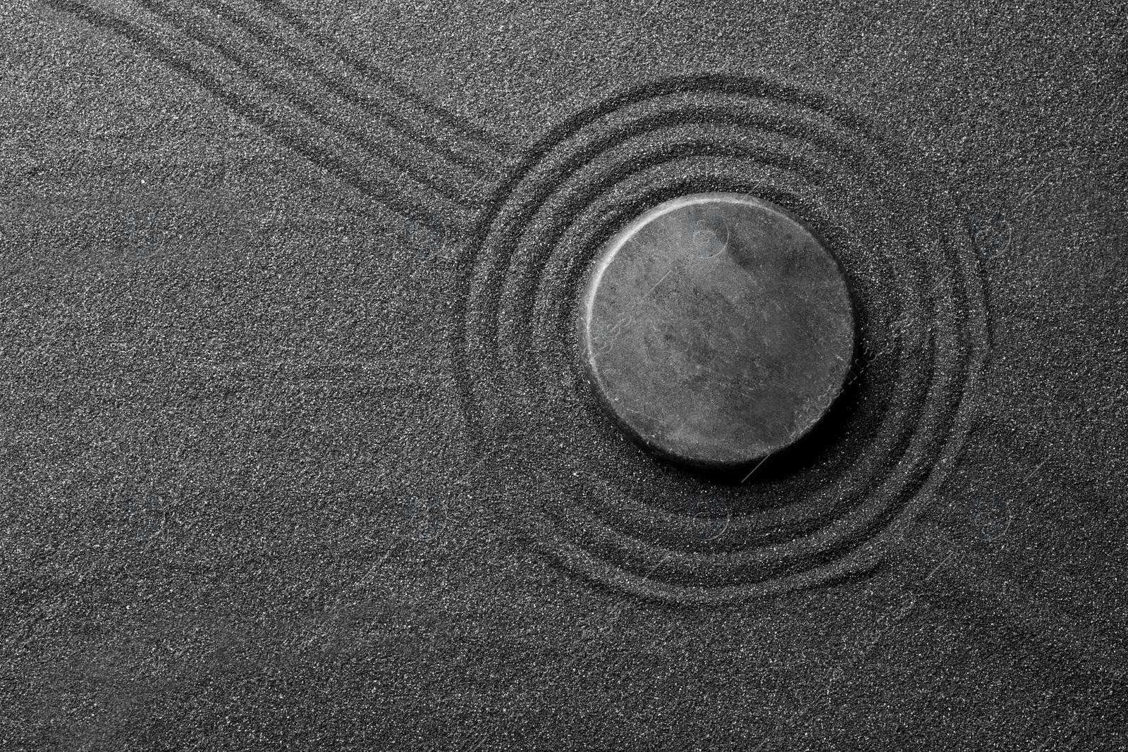 Photo of Zen garden stone on black sand with pattern, top view