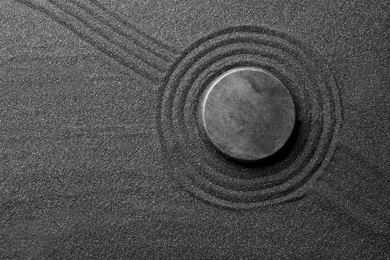 Photo of Zen garden stone on black sand with pattern, top view