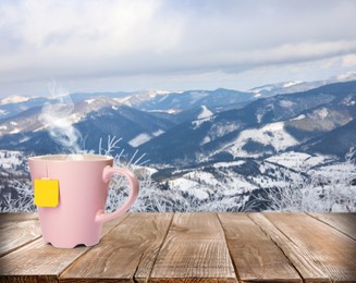 Image of Cup of hot tea on wooden table and beautiful winter landscape on background