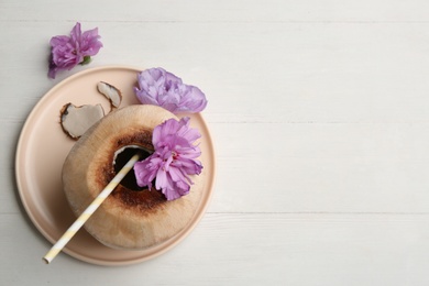 Photo of Young peeled coconut with straw and flowers on white wooden table, flat lay. Space for text