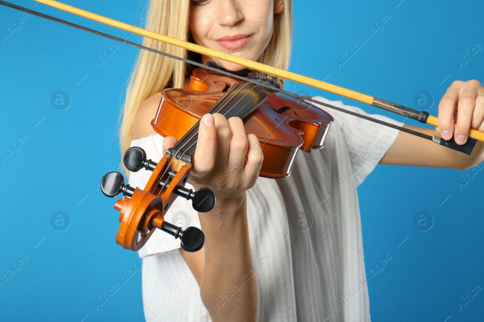 Photo of Beautiful woman playing violin on light blue background, closeup