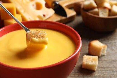 Photo of Dipping piece of bread into tasty cheese fondue at table, closeup