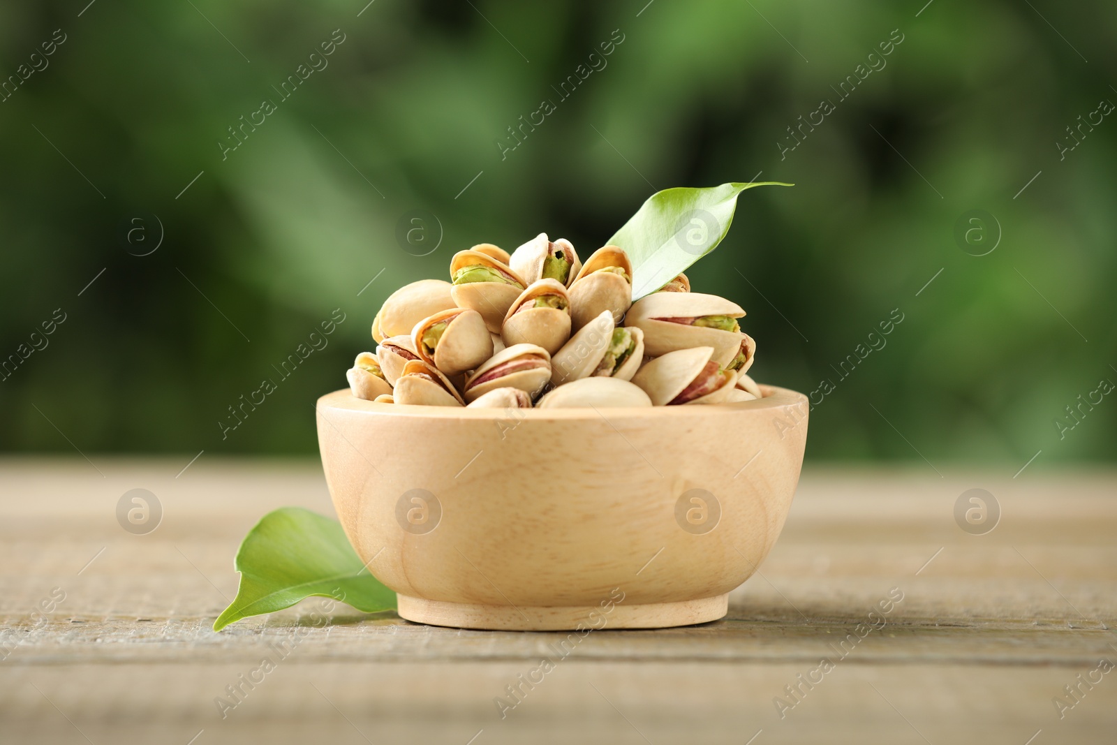 Photo of Tasty pistachios in bowl on wooden table against blurred background, closeup