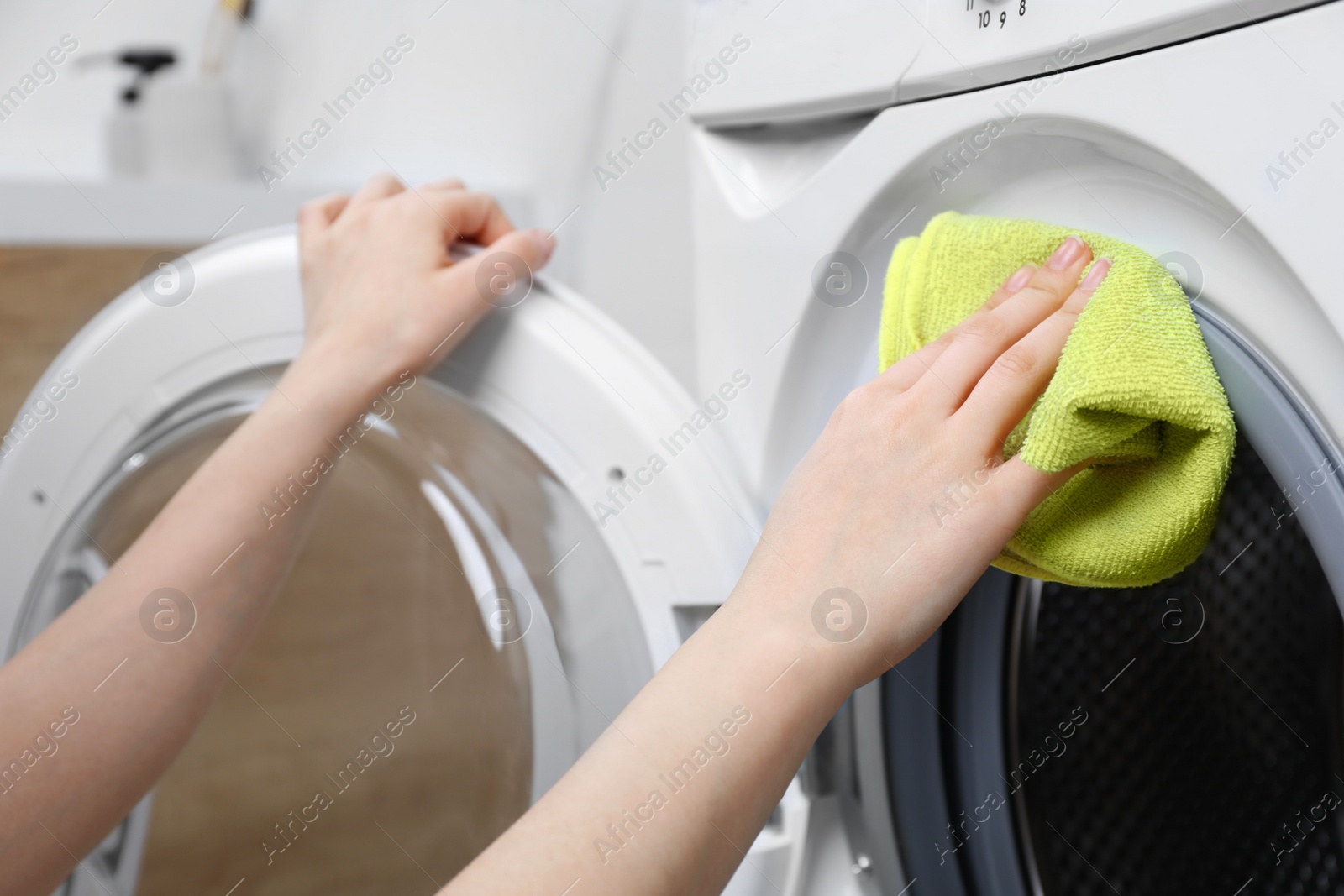 Photo of Woman cleaning washing machine with rag indoors, closeup