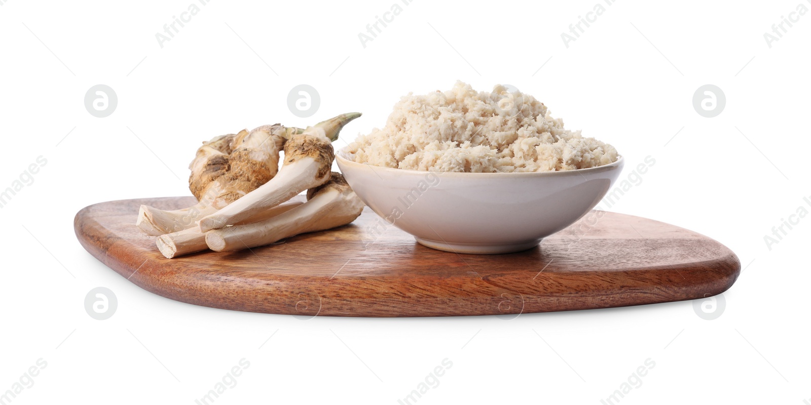 Photo of Wooden board with bowl of tasty prepared horseradish and roots isolated on white