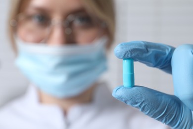 Doctor holding pill on light background, selective focus. Space for text