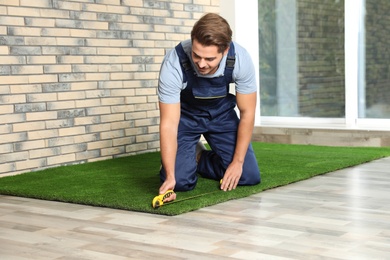 Photo of Man in uniform cutting artificial grass carpet indoors