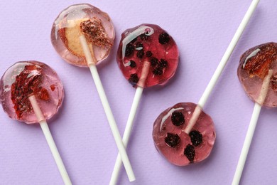 Sweet colorful lollipops with berries on lilac background, flat lay