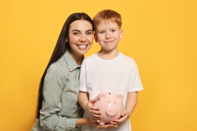 Photo of Mother and her son with ceramic piggy bank on orange background
