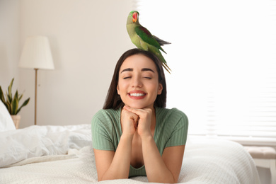 Photo of Young woman with Alexandrine parakeet indoors. Cute pet