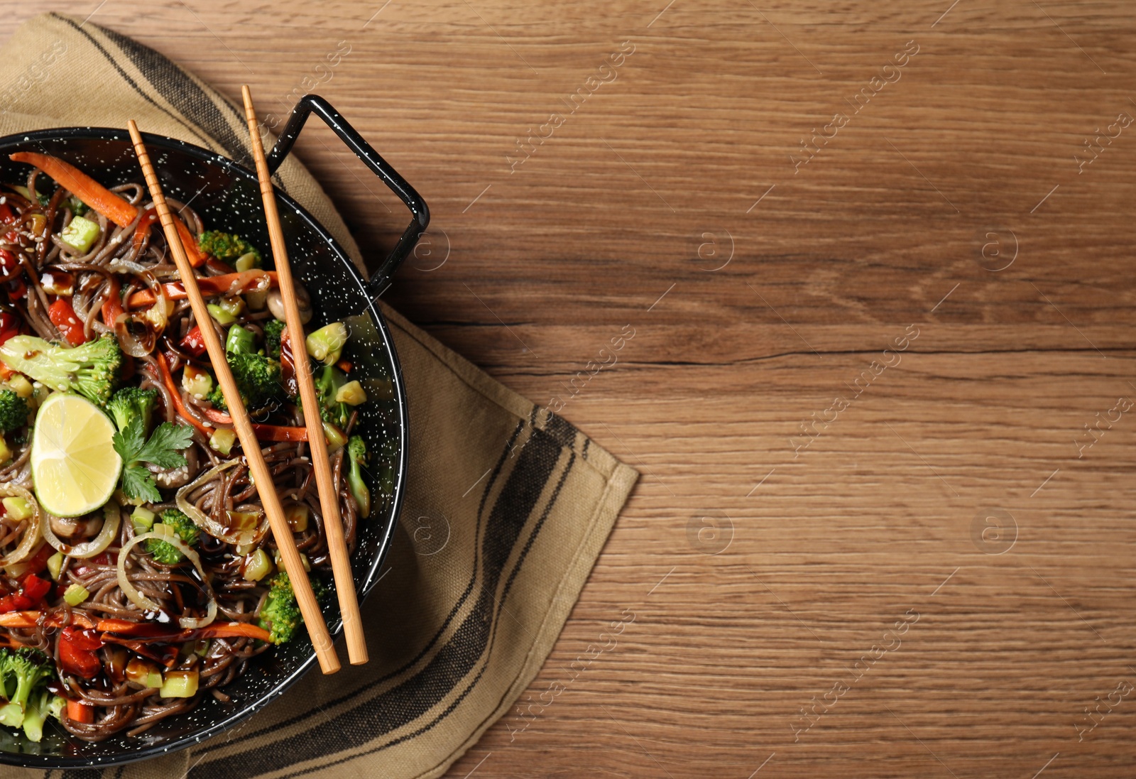 Photo of Stir-fry. Tasty noodles with meat in wok and chopsticks on wooden table, top view. Space for text